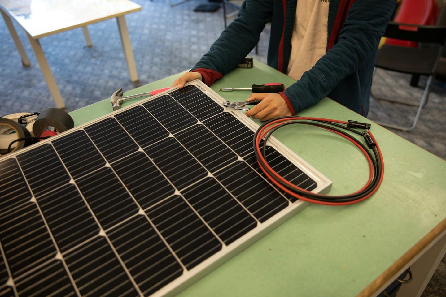 A worker uses pliers to assemble a solar panel at a workbench.